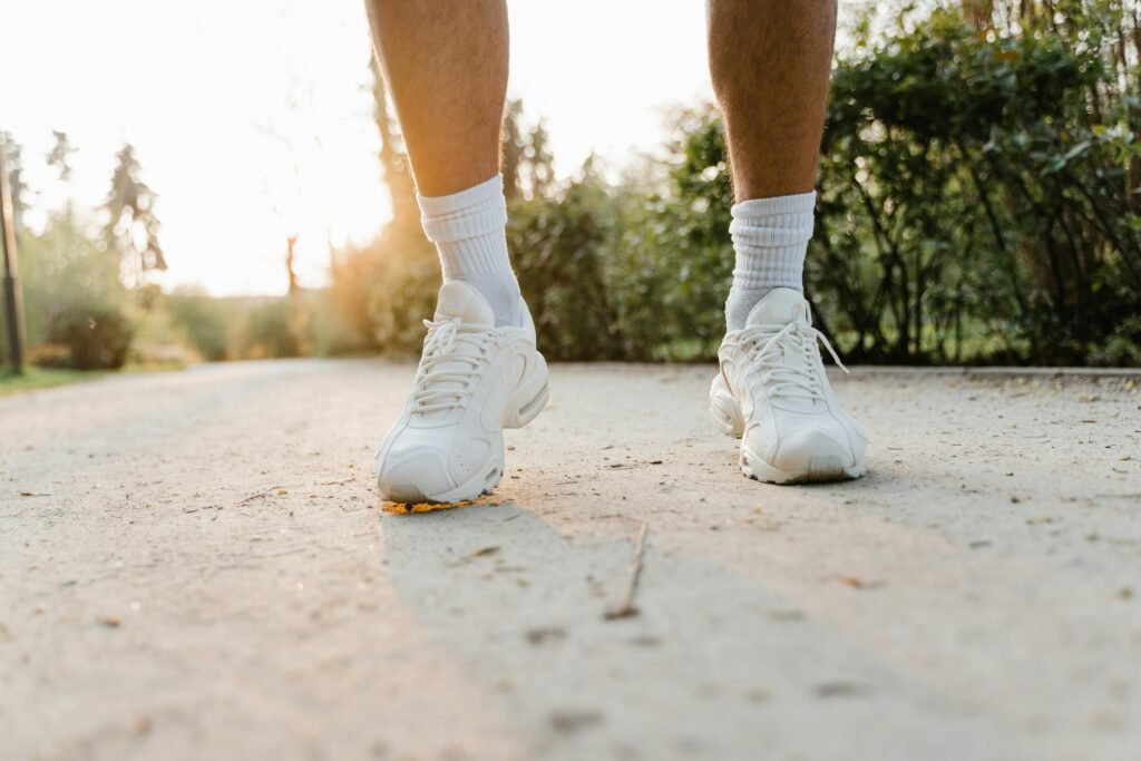 pexels-photo-7880267-7880267 Close-up of legs wearing white sneakers walking on a sunlit path outdoors.